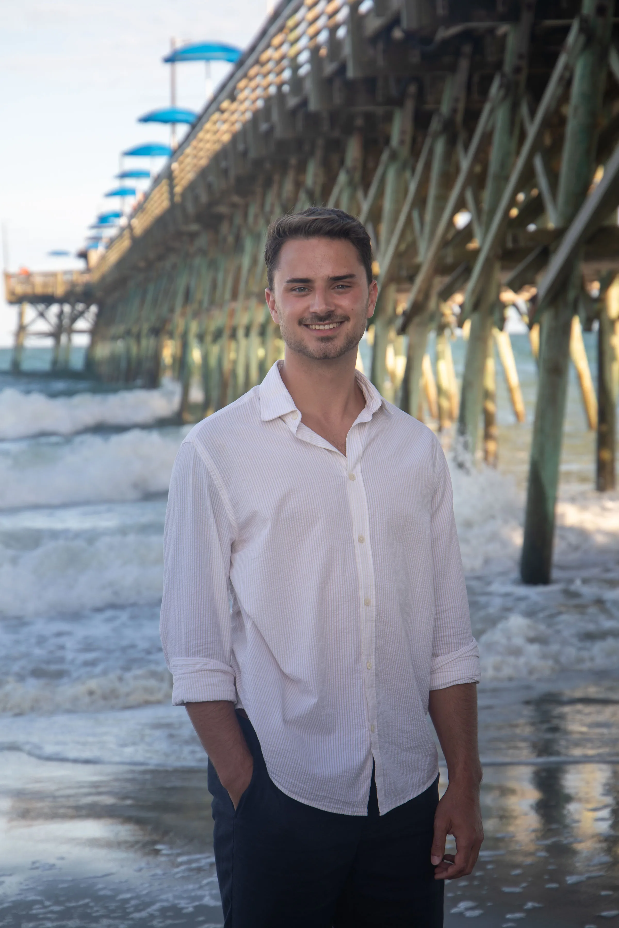 Portrait of Jacob Tolar standing on the beach beside a pier
